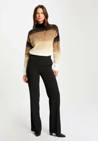 Suéter con rayas en degradado de negro, marrón y crema, cuello redondo y mangas largas. Combinado con pantalones negros de cintura alta y zapatos de punta.