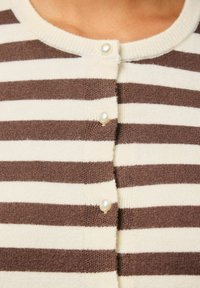 Gestreepte cardigan in roomkleur en bruin, met een ronde halslijn, knoopsluiting aan de voorkant met parelachtige knopen en een zachte brei-textuur.