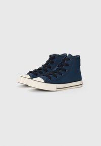 Baskets montantes en toile navy avec lacets noirs, capucho en caoutchouc blanc et coutures détaillées. Elles présentent une surface texturée et des accents noirs.