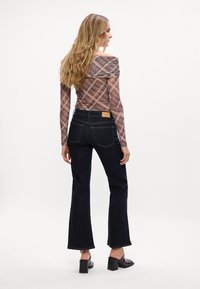 Dolga rokav, off-shoulder karirasta bluzica iz prosojnega materiala, v kombinaciji z visokim pasom temno modrim razširjenim jeansom z teksturo in šivanjem.