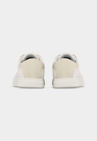 Paire de baskets Calvin Klein blanches et beiges vues de dos sur un fond blanc uni.