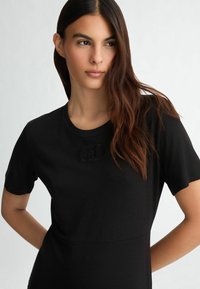 Black short-sleeve shirt with a round neckline and subtle logo detail on the chest, made from smooth, lightweight fabric.