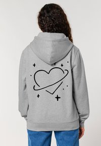 Pilkas džemperis su gobtuvu, pagamintas iš minkštos medžiagos, ant nugaros didelė juoda širdies grafika su žvaigždėmis. Ribuoti rankogaliai ir kraštas, erdvus gobtuvas.