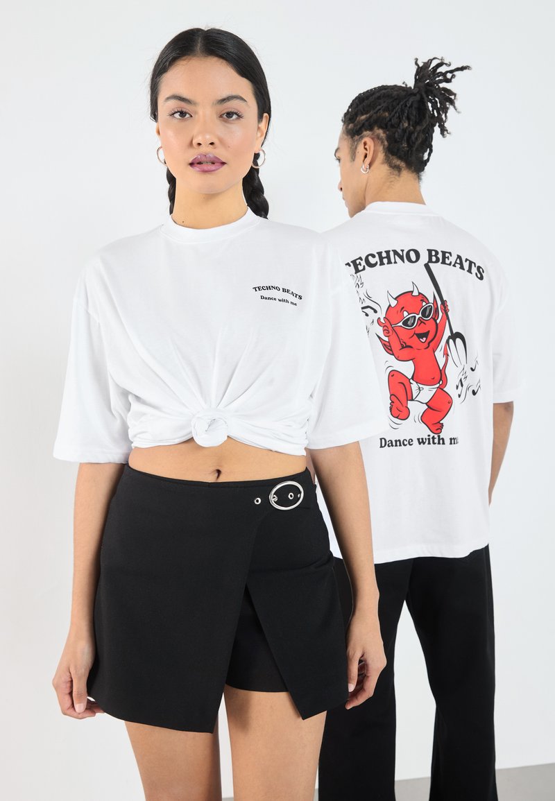 Balta per didelį t-shirt su priekyje mazgu, su raudonos velnio grafika ir tekstu nugaroje. Juoda apvyniojama sijonas su sidabrinėmis apvalios detalėmis.