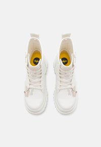 Witte enkellaarsjes met vetersluiting, ronde neus en chunky zool; heeft pastel vlinderaccenten aan de zijkant en een gele inlegzool.