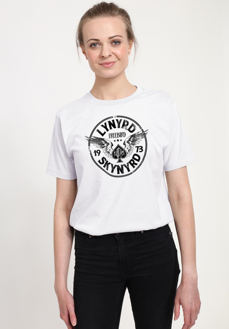 Hvid bomulds t-shirt med et sort grafisk design, der har teksten "Lynyrd Skynyrd Freebird 1973" og vinge-symboler, korte ærmer, rund hals.