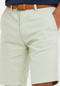 Pantalones cortos verde claro hechos de una mezcla de algodón, con bolsillos laterales, detalles cosidos y un cinturón tejido marrón.