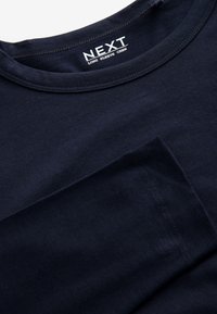 T-shirt bleu marine à manches longues avec col rond, coutures visibles au niveau du col et des manches, étiquette "NEXT LONG SLEEVE CREW" à l'intérieur du col.