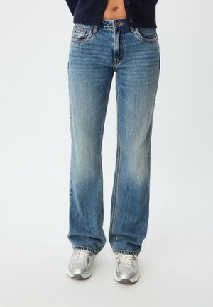 Onderlichaam met lichtblauwe rechte jeans en zilveren sneakers, gecombineerd met een donkerblauwe cropped trui.