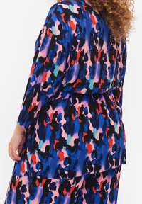 Maglietta multicolore a maniche lunghe con un audace motivo astratto in nero, blu, rosso e rosa. Tessuto morbido e scivoloso con una vestibilità rilassata.