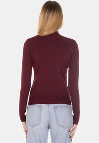 Maglione bordeaux a maglia con design aderente, maniche lunghe e orlo a coste. Abbinato a jeans azzurri a vita alta.