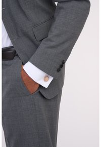 Grauer Anzug mit strukturierter Oberfläche, weiße Hemdmanschetten mit einem goldenen Akzentknopf und schwarzen Knöpfen an den Ärmeln.