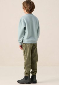 Lichtblauwe sweatshirt met ribgebreide manchetten, gecombineerd met losse olijfgroene pants en donkergrijze enkelboots, gezien vanaf de achterkant.