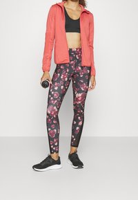 Tenue sportive comprenant une veste zippée corail, un crop top noir, des leggings à motifs floraux et des chaussures de sport noires.