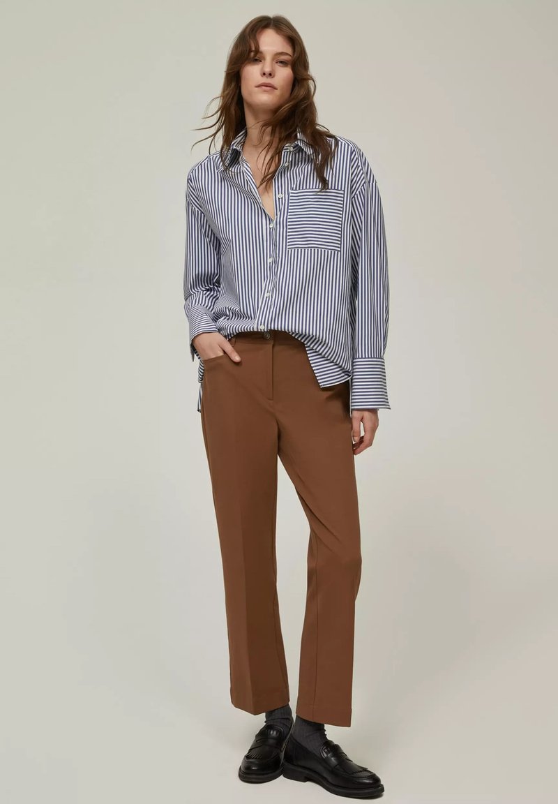 Camicia a strisce blu e bianche con taschino abbinata a pantaloni dritti marroni e mocassini neri. Tessuti morbidi.