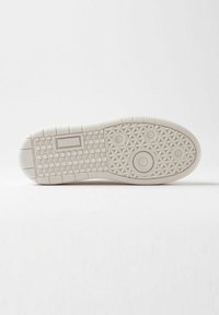 Sålen af en beige sneakers med geometriske mønstre, cirkulære indrykninger og et rektangulært logo, der siger "D.A.T.E." på en hvid baggrund.