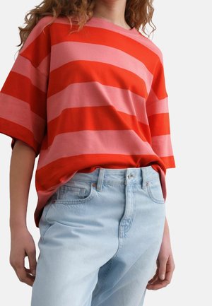 Person trägt ein lockeres rot-rosa horizontal gestreiftes Kurzarmshirt, das in hellblaue, hoch taillierte Jeans gesteckt ist.