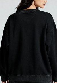 Felpa nera oversize con colletto e polsini a costine, realizzata in un tessuto testurizzato e con un discreto logo sul retro.