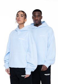 Sudaderas de color azul claro fabricadas en una tela suave, con un bolsillo frontal y el logo blanco "MULTIPLY". Se combinan con pantalones de chándal negros que exhiben una marca a juego.