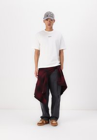 Hvid kortærmet t-shirt med "REPLAY" logo, mørkegrå cargo-bukser, sort og rødternet skjorte bundet om livet, grå kasket, brune sneakers.