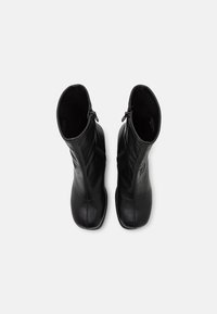 Botas de cuero negro hasta el tobillo con una textura suave, forma cónica y cremalleras laterales para el cierre, con detalles de costura mínimos.