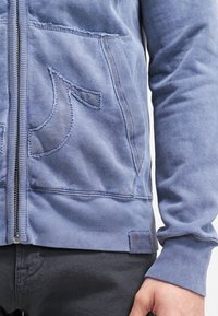 Felpa con cappuccio blu con zip, realizzata in tessuto morbido, con una grande tasca frontale decorata da un ricamo e polsini a coste.