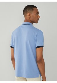 Polo shirt azzurro chiaro con tessuto testurizzato, maniche corte e dettagli blu navy sul colletto e sui polsini. Caratterizzato da fessure laterali.