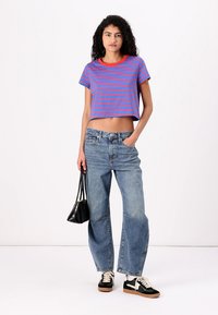Beskarvet t-skjorte med blå og rosa horisontale striper, rød hals, kombinert med lyseblå vide jeans og svarte joggesko. Liten svart håndveske.