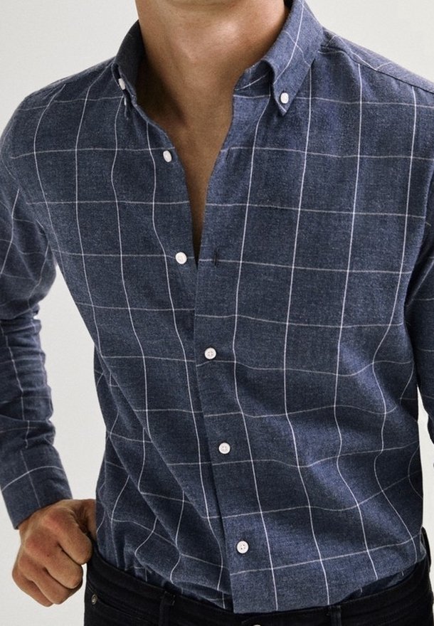 Chemise à carreaux bleus en tissu texturé ; dotée d'un col pointu et de boutons blancs, avec un motif en grille sur toute la surface.