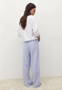 Top bianco a maniche lunghe abbinato a pantaloni da pigiama larghi a strisce blu e bianche, caratterizzati da una vita elasticizzata e una vestibilità comoda.