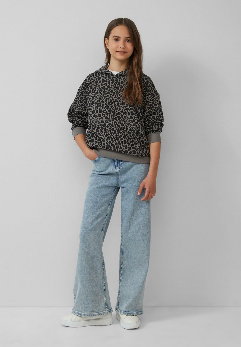 Dunkelgrauer Sweatshirt mit schwarzem Leopardenmuster, ausgestattet mit Kapuze und gerippten Bündchen. Kombiniert mit hellblauen weit geschnittenen Jeans und weißen Sneakern.