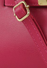 Roze handtas van textuurmateriaal met een gouden vierkante metalen accent. Voorzien van zichtbare stikdetails en een ritssluiting.