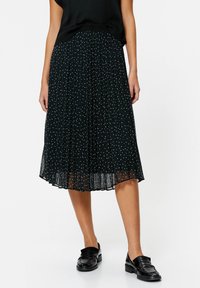 Sort plisseret nederdel med hvide prikker, gennemsigtig stof, ankel-længde, med et luftigt design. Båret med sorte loafers.