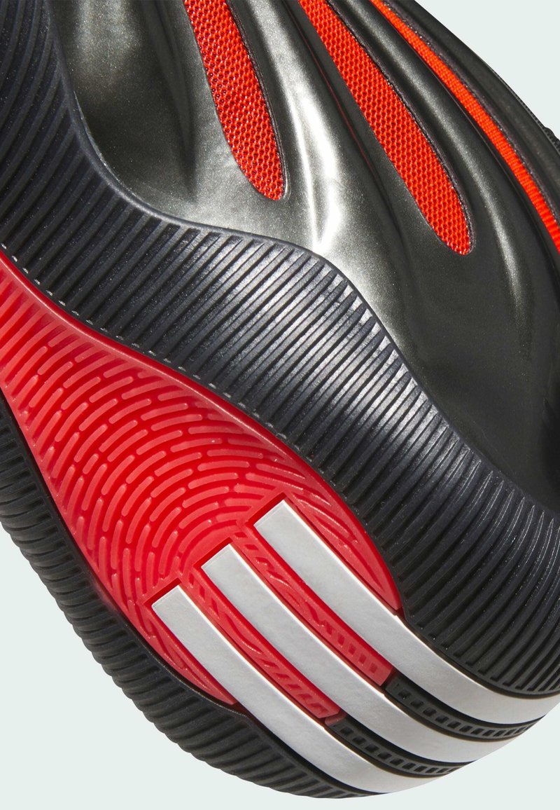 Baskets de sport noires avec accents en maille rouge, tige en texture lisse et semelle en caoutchouc noire et rouge au motif distinctif avec des rayures blanches.