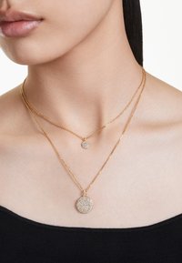 Kullatud kaelakeed, mis sisaldavad väikest ringikujulist ripatsit ja suuremat, tekstuurset ümmargust ripatsit, millel on sädelevad aktsendid.