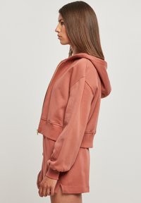 Støvete rose cropped hettegenser med glidelås foran, overdimensjonerte ermer og matchende shorts. Mykt stoff med en jevn tekstur og uten mønstre.