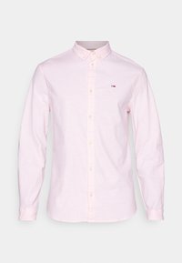 Hellrosa Langarmhemd mit Knopfverschluss, das auf der linken Brust ein kleines rechteckiges Logo in Rot, Weiß und Navy sowie einen Button-down-Kragen aufweist.