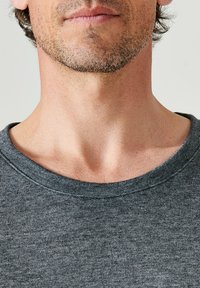 Grijze katoenen T-shirt met een ronde halslijn, met een zachte textuur en een ruime pasvorm, waarbij de nek- en schouderpartij van dichtbij wordt getoond.