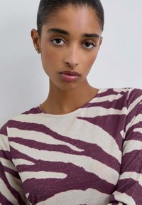 Camiseta de manga larga en crema con rayas de cebra color burdeos, que presenta un escote redondo y una textura suave con sutiles toques de brillo.
