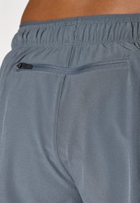 Gray athletic shorts with a smooth texture, featuring a zippered pocket and small perforations for breathability. Elastic waistband.