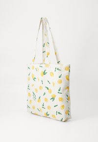 White canvas tote bag with all-over yellow lemon and green leaf pattern, shown standing with straps extended against a plain background.