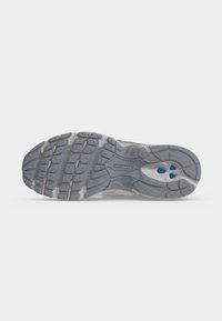 Σόλα από γκρι παπούτσι τρεξίματος New Balance με υφή πέλματος και μπλε λεπτομέρειες στην περιοχή της φτέρνας.