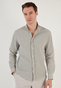 Camisa de botones a rayas en verde y blanco. Presenta un cuello, mangas de longitud completa y un diseño ajustado con una textura sutil.