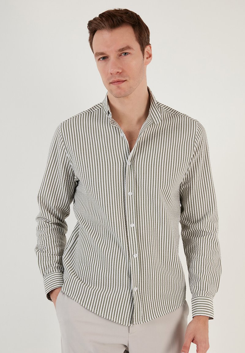 Camisa de botones a rayas en verde y blanco. Presenta un cuello, mangas de longitud completa y un diseño ajustado con una textura sutil.