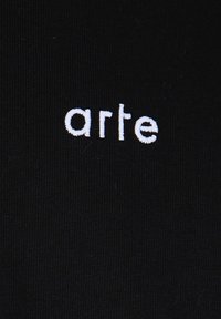 Tessuto nero con texture a coste che presenta la scritta "arte" in lettere ricamate bianche centrata sulla superficie.