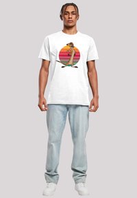 Hvit bomull T-skjorte med et tegneseriefigur foran en flerfarget solnedgangsirkel. Kombinert med lyse denimjeans og hvite sneakers.