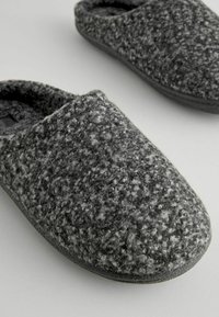Graue Filzschlappen mit strukturierten Oberflächen, abgerundeter Zehenpartie und weicher Innenauskleidung. Schwarze Gummisohle für Langlebigkeit.
