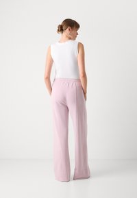 Light pink, wide-leg trousers with an elastic waistband and a smooth texture, paired with a white sleeveless top featuring a scalloped edge.
