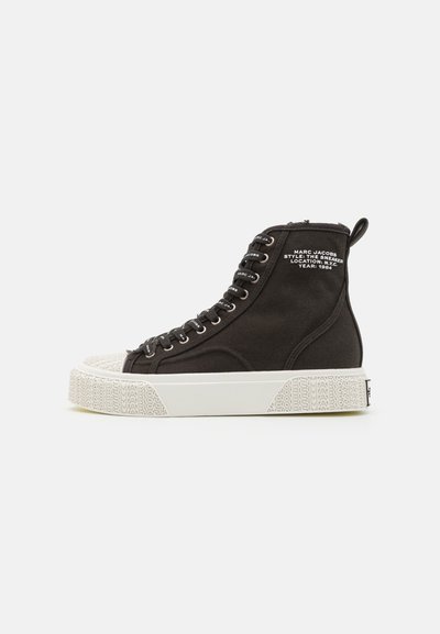 Sneaker neri alti in tela con suola in gomma bianca. Presenta occhielli argentati, lacci neri e un marchio sul lato. Punta strutturata.