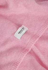 Maglione in cashmere rosa chiaro con colletto a coste e un'etichetta bianca con "AMERICA TODAY." Tessuto morbido, leggermente stropicciato.